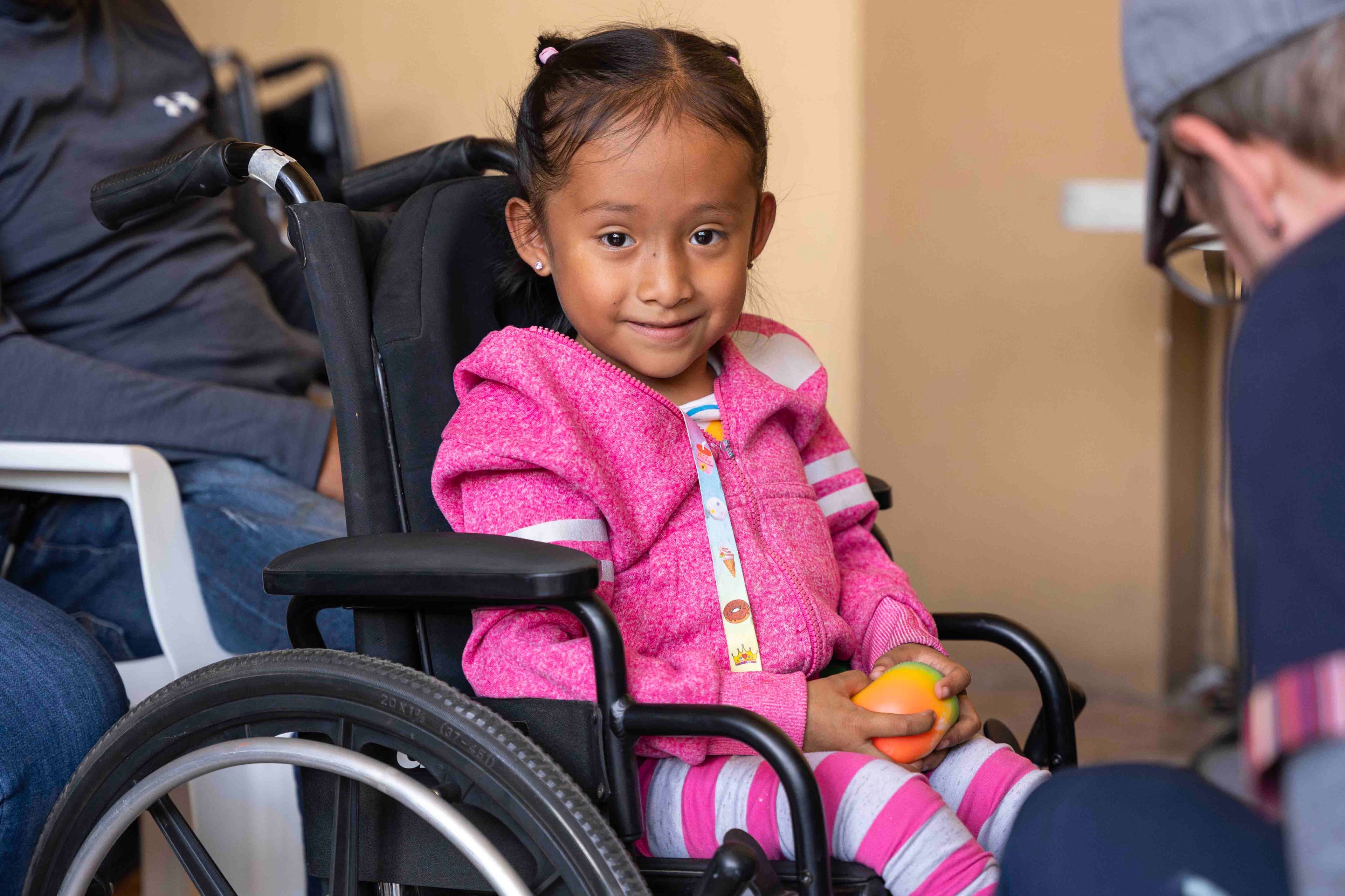 A little girl in her new wheelchair smiling joyfully for the camera.