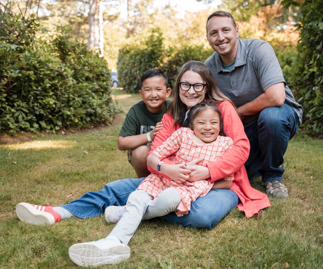 A family of four smiles while posing together on the grass.