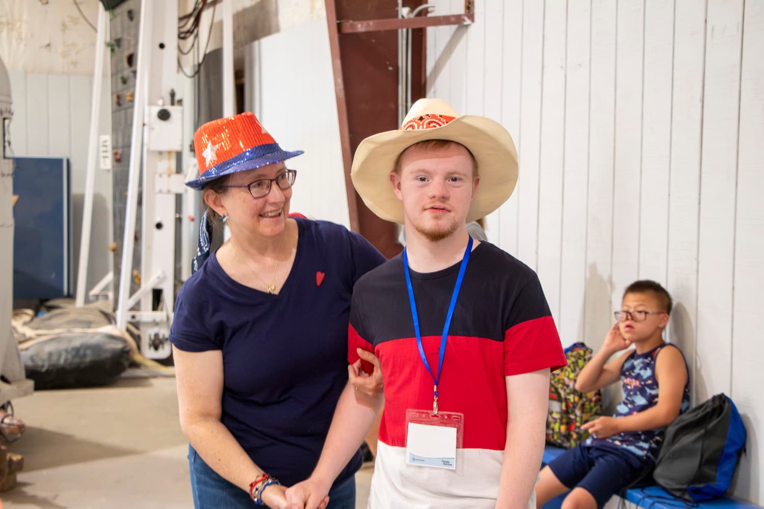 A man with a disability wearing a cowboy hat stands next to a smiling woman, also in a cowboy hat, who is looking at him.