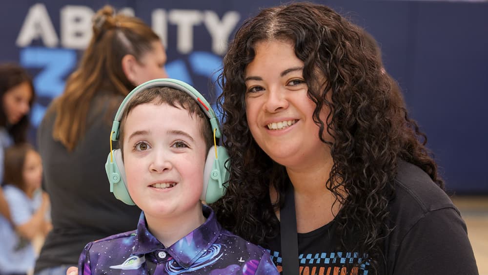 A young boy wearing headphones smiles beside a woman who is also smiling.