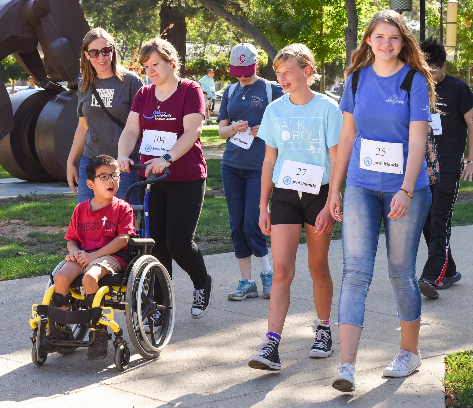 A group of people wearing number tags walk in an event alongside a boy in a wheelchair.