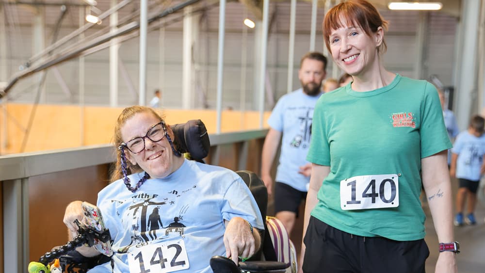 A woman in a wheelchair with another woman beside her. Both are smiling for the camera. 