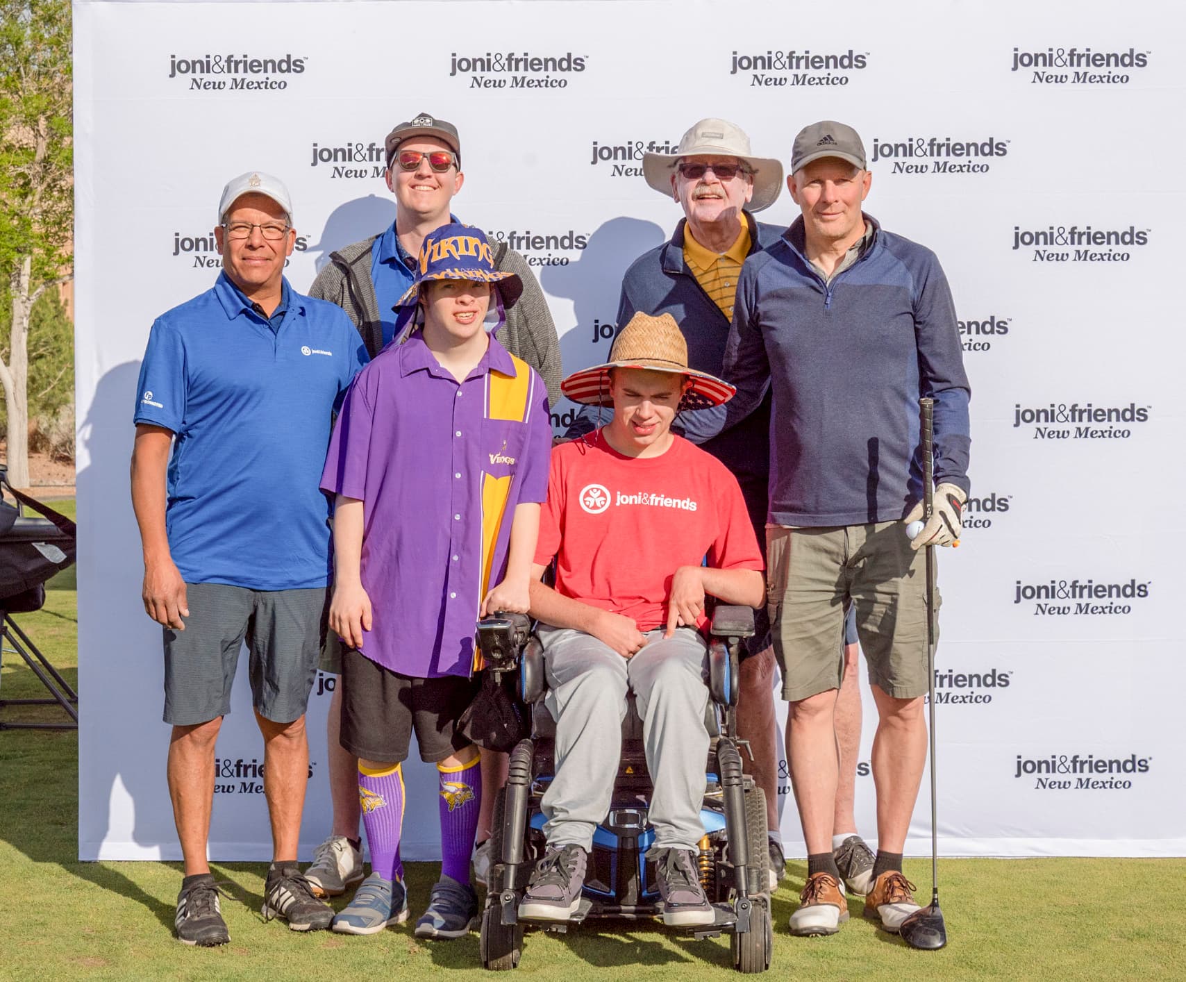 Five men stand in front of a banner reading "Joni & Friends New Mexico," while one man in a wheelchair smiles and poses for the camera.
