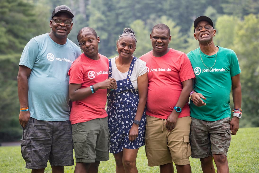 A family of five smiling and posing outdoors on a green field with trees in the background.