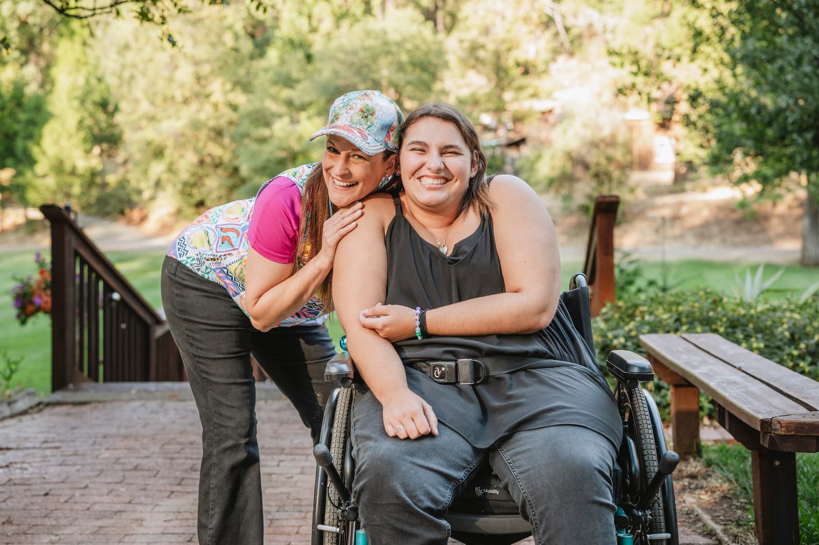 A woman in a wheelchair next to another woman. Both are smiling for the camera.