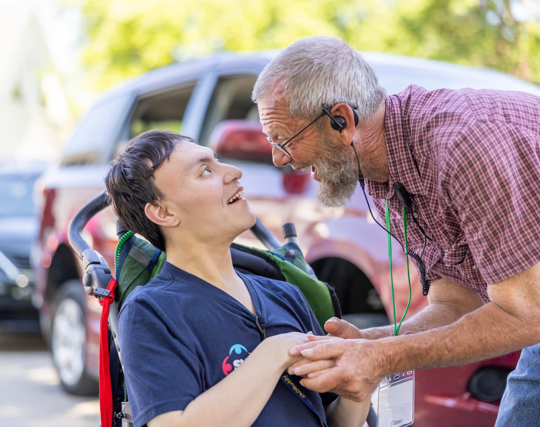 A man with a disability looking at another man; both are smiling and looking at each other.