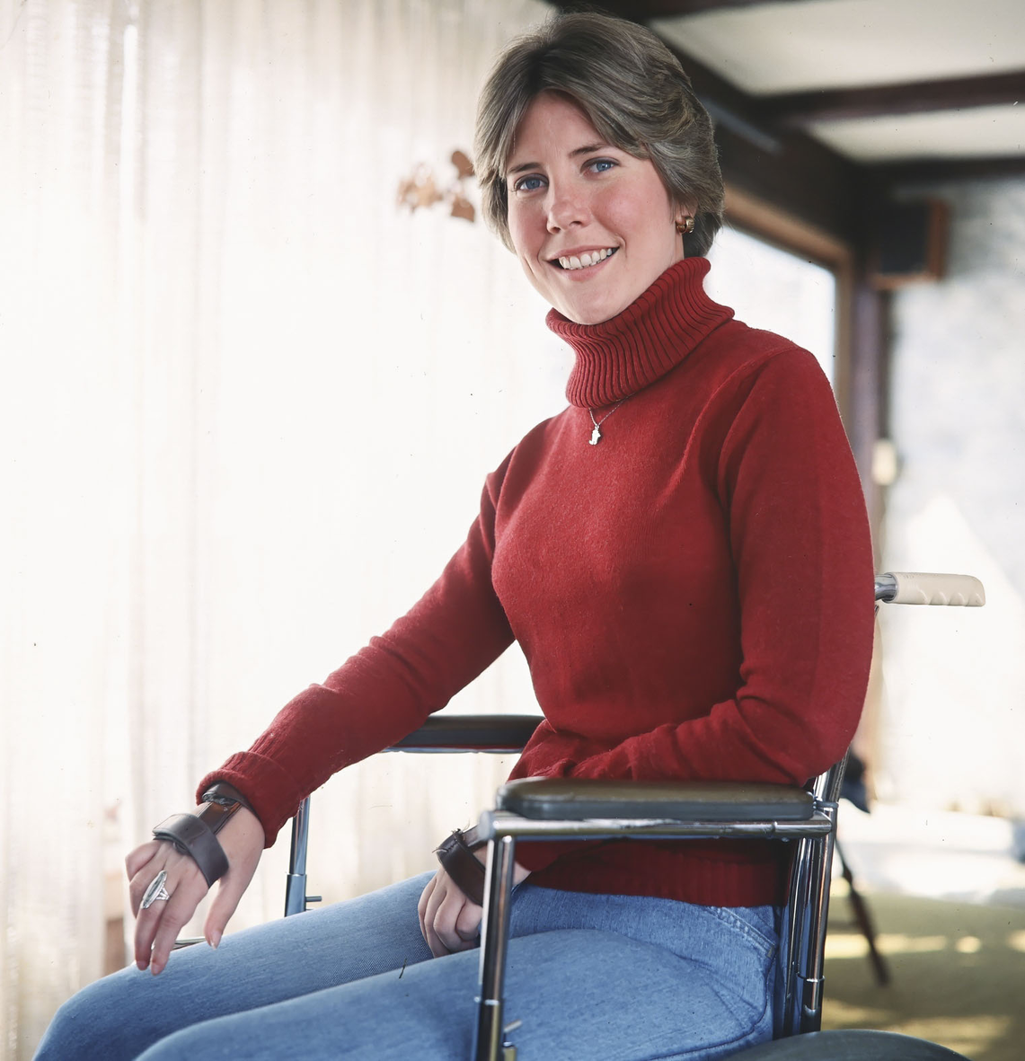 Young Joni Eareckson Tada sitting in her wheelchair and smiling for the camera. 