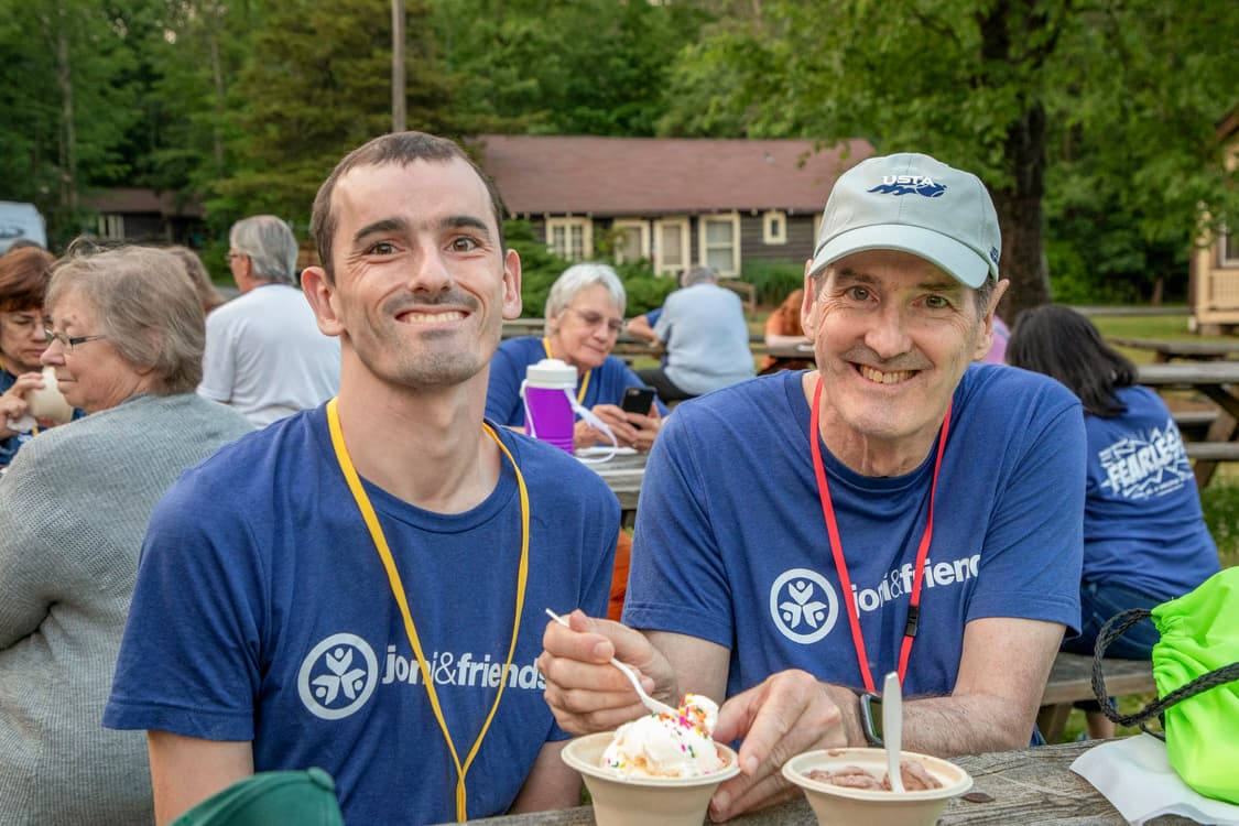 A man eating ice cream with his dad with other people in the background. 