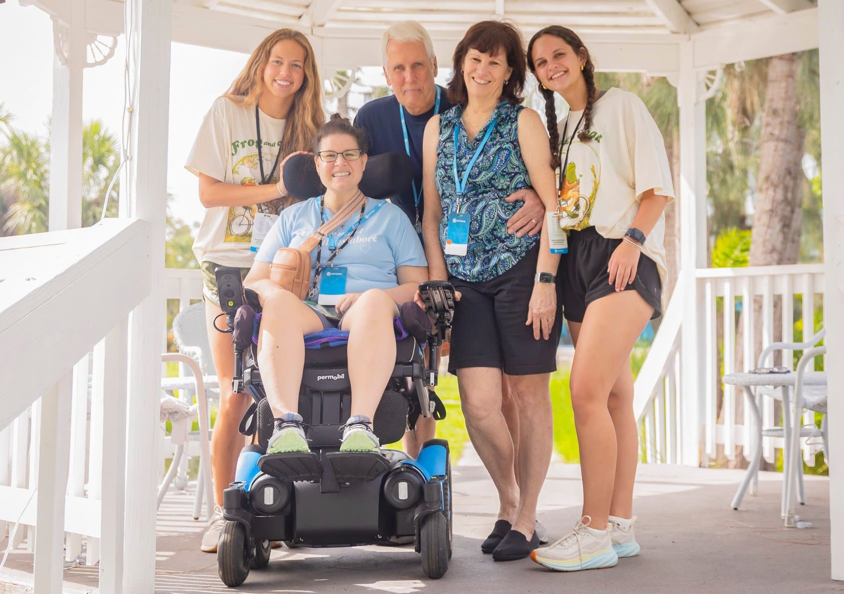 A group of five people smiles under a gazebo. One person is in a wheelchair, while the others stand around, creating a warm, friendly atmosphere.