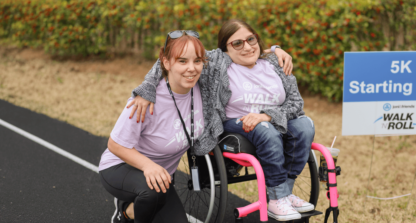 A group of people wearing number tags walk in an event alongside a boy in a wheelchair.