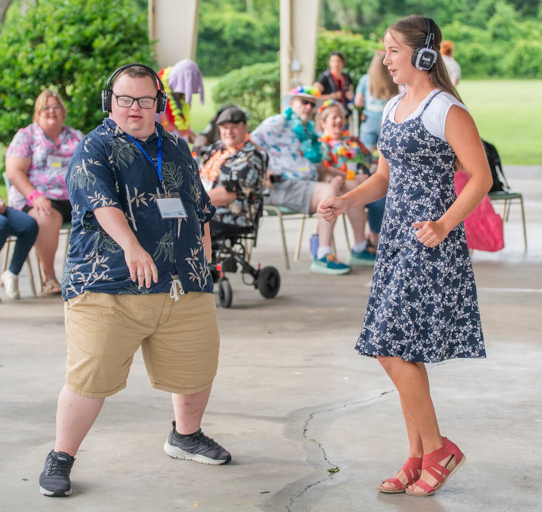 Two people with headphones dancing in the middle with people in the background watching them while sitting.