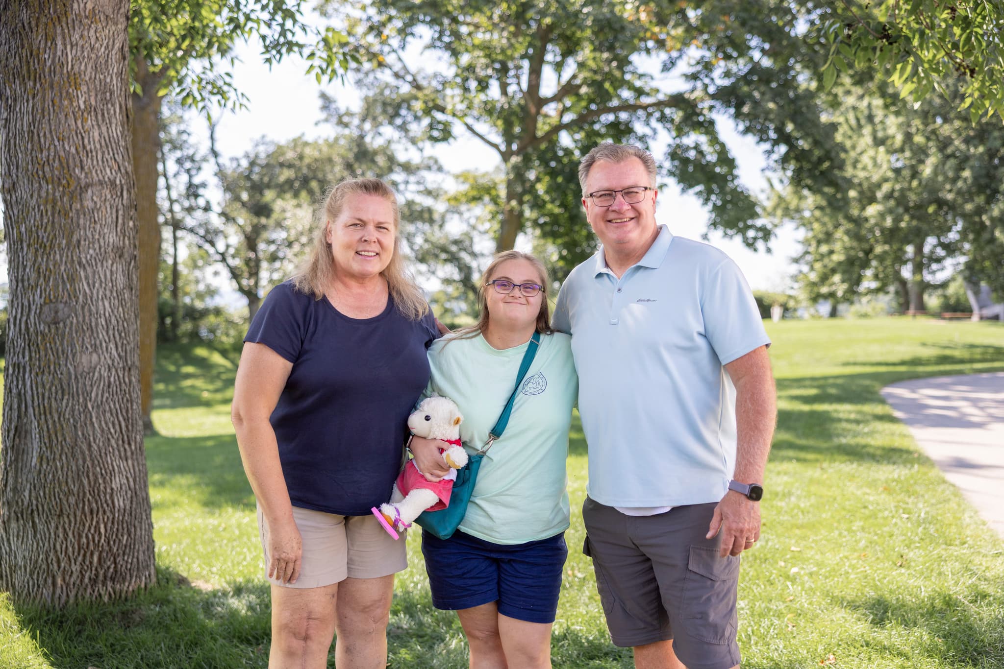 A young girl with a disability smiling alongside her parents in a sunny outdoor setting.