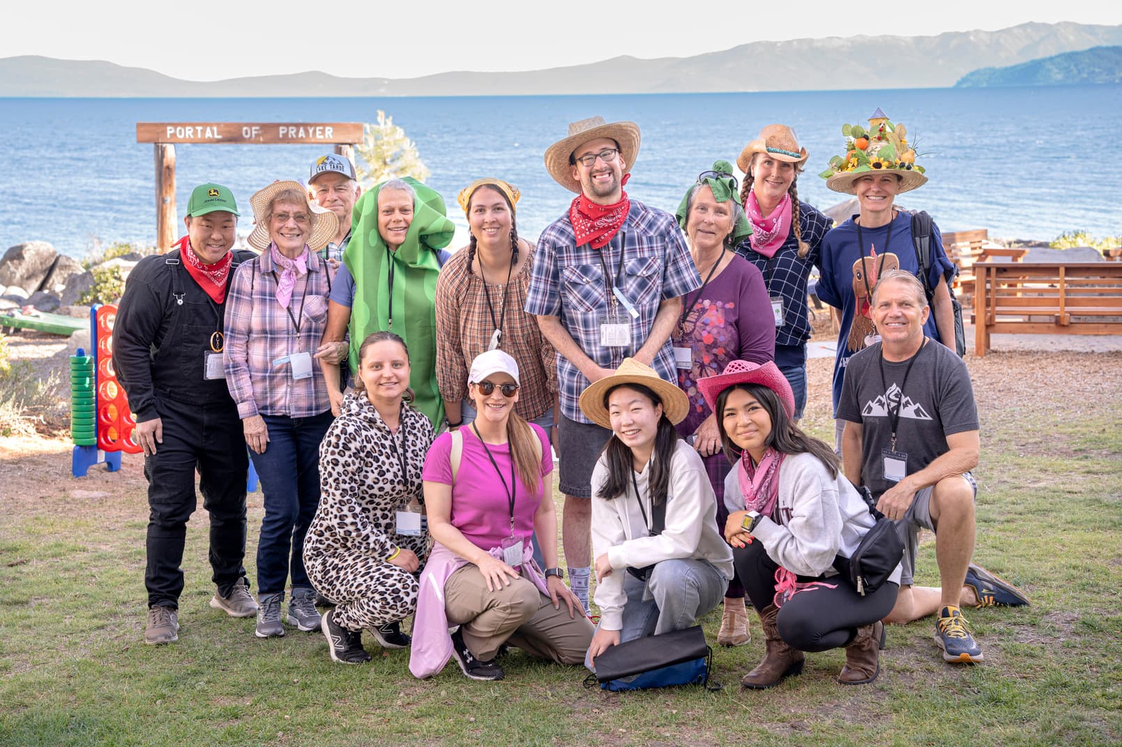 A group of people wearing colorful straw hats and cowboy costumes, smiling and posing together in front of a bay.