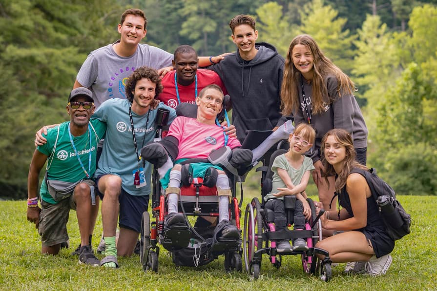 A group photo with two people using wheelchairs and several others on grass, with trees in the background.