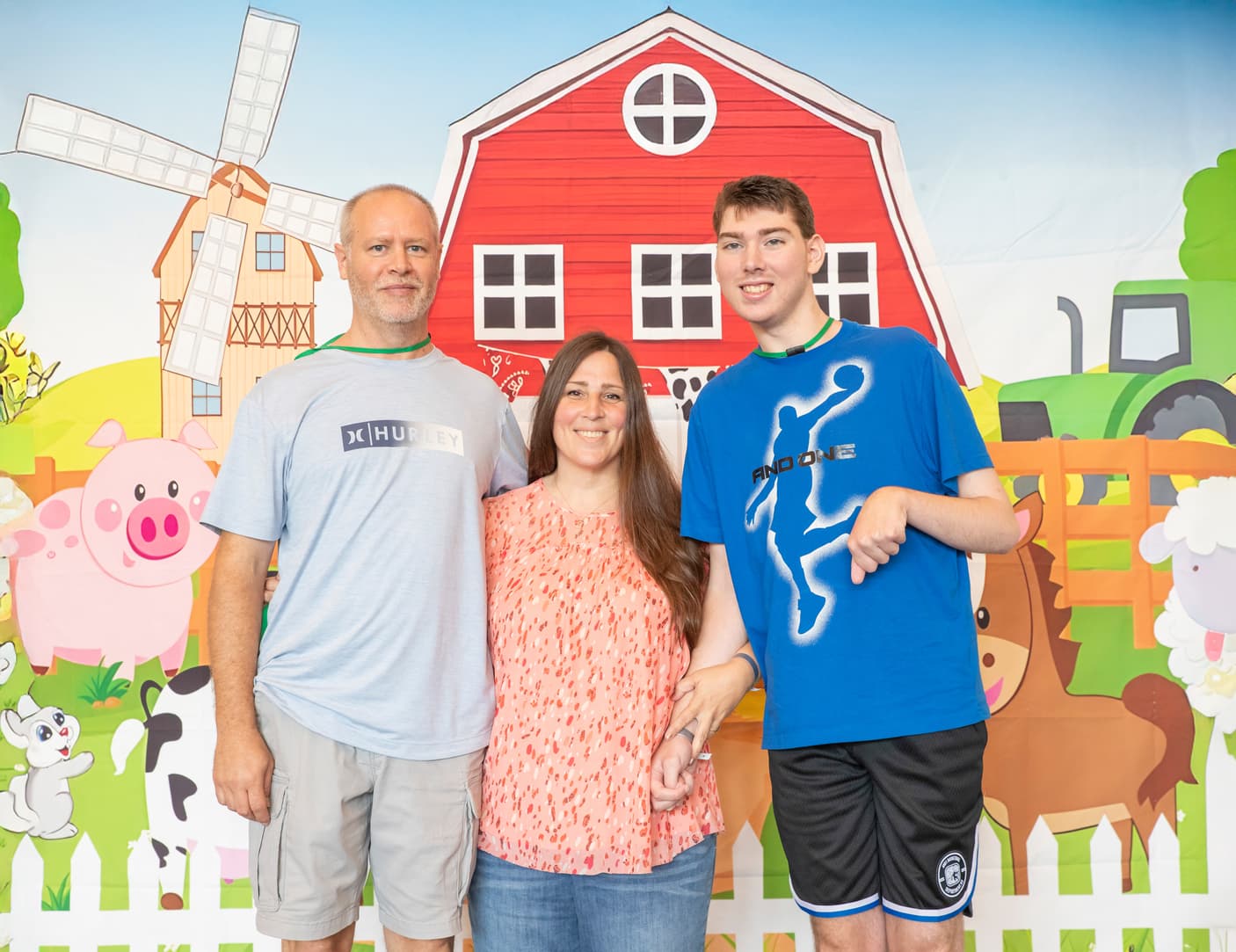 A mother and father posing with their son, who has a disability, in front of a cute illustrated barn backdrop