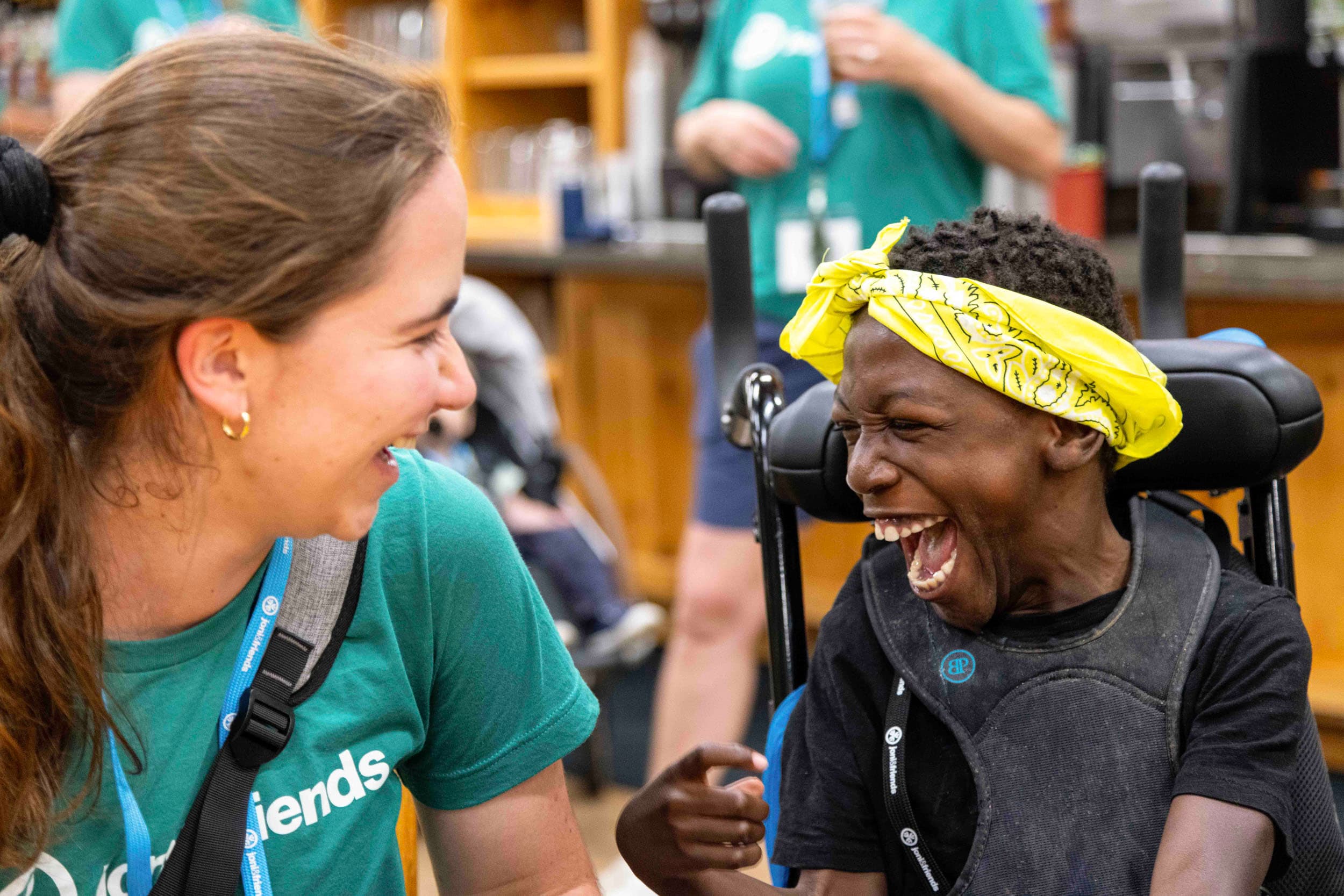 A volunteer smiling at a boy in a wheelchair as they laugh and enjoy a joyful moment together.