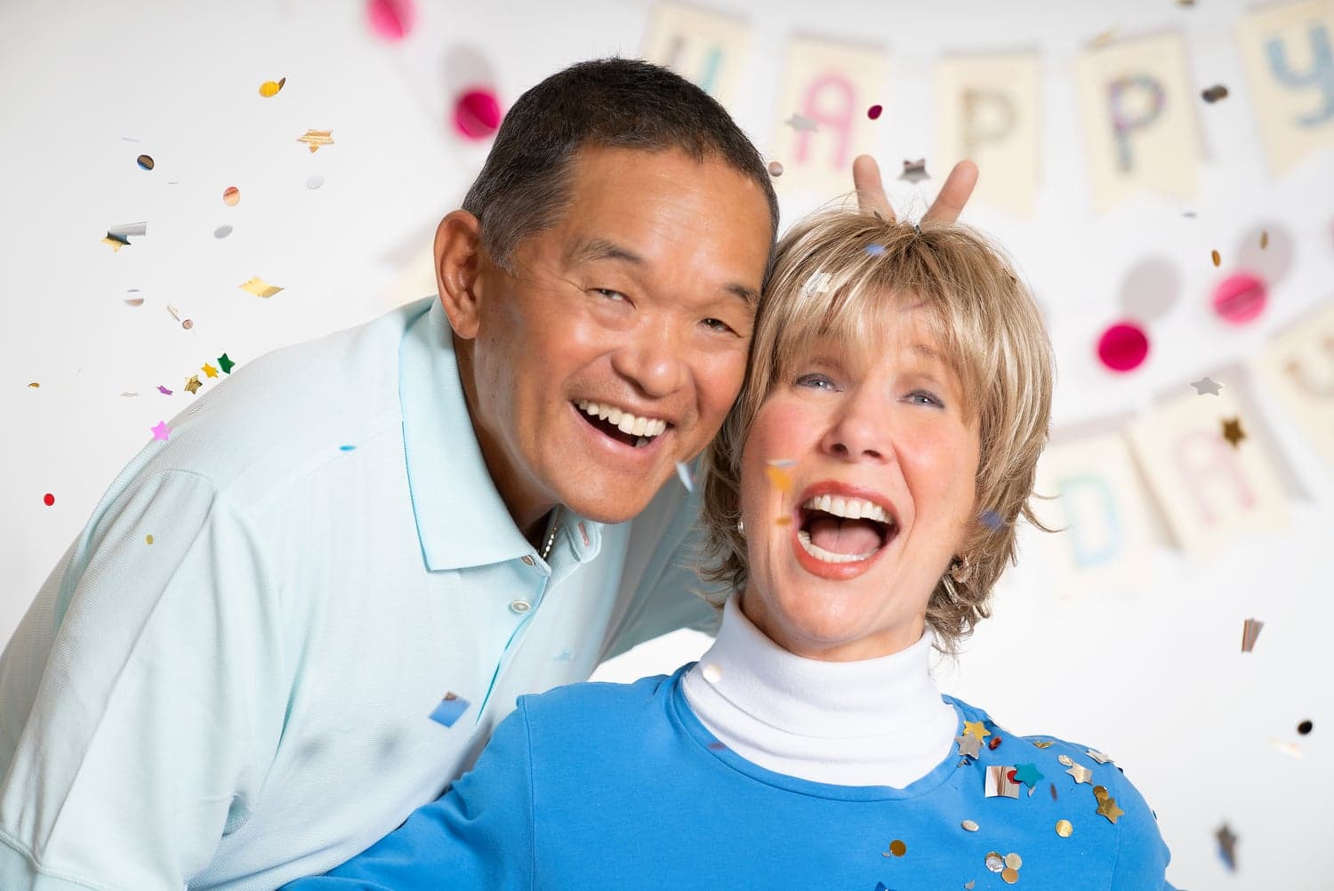 Joni and Ken smiling at the camera, surrounded by confetti and "Happy Birthday" letter flags.