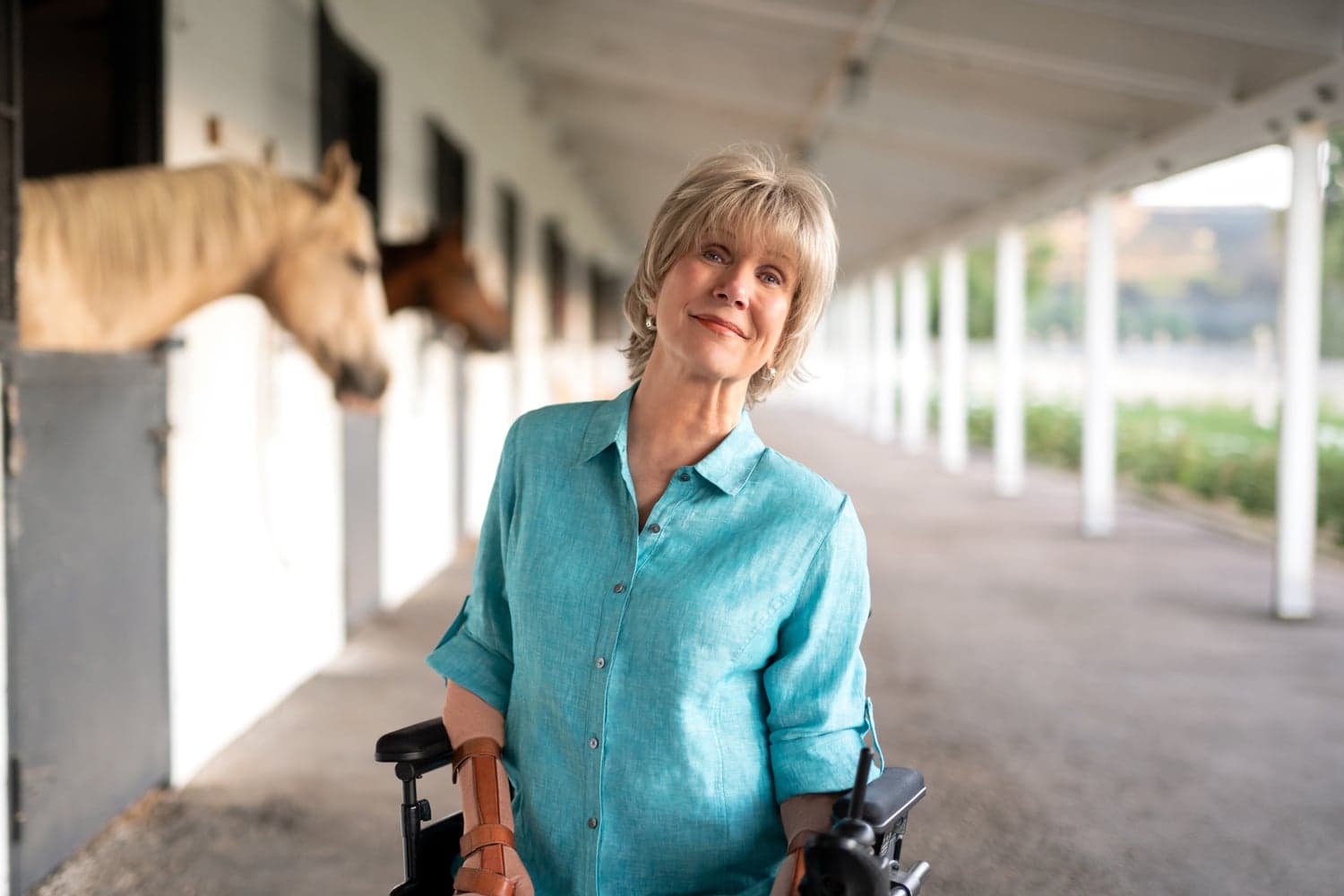 A clearer version would be:
Joni Eareckson Tada smiling for the camera with two horses inside their enclosure.