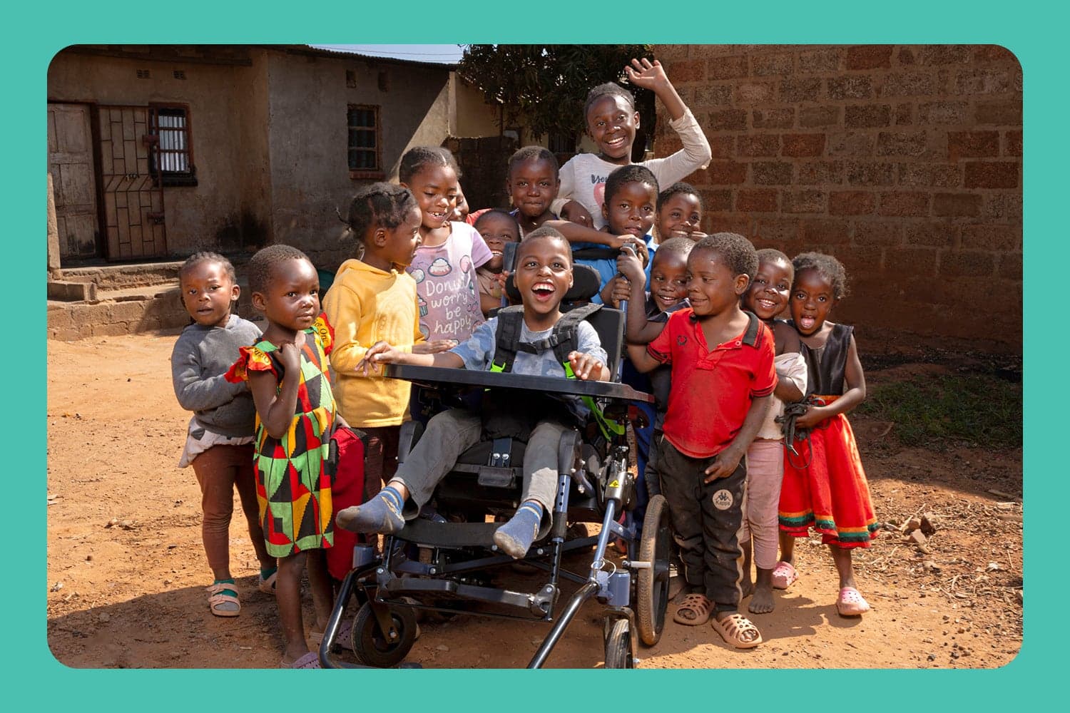 A child in his new wheelchair surrounded by other smiling children, all looking happy and excited.